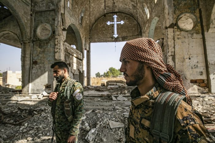 Members of the Khabour Guards (MNK) Assyrian Syrian militia, affiliated with the Syrian Democratic Forces (SDF), walk in the ruins of the Assyrian Church of the Virgin Mary, which was previously destroyed by Islamic State (IS) group fighters, in the village of Tal Nasri south of the town of Tal Tamr in Syria's northeastern Hasakah province on November 15, 2019. - The few Assyrian Christians who escaped the Islamic State group invasion in 2015, and did not choose to emigrate, now anxiously watch the advance of Turkish forces toward their villages in southern Hassakeh province. Ankara is still trying to gain ground despite two ceasefire agreements reached last month to put an end to its offensive against the Kurdish-dominated region. Turkey had launched the offensive on October 9 to push back from its border the Kurdish People's Protection Units (YPG), the backbone of the Kurdish-Arab Syrian Democratic Forces (SDF), and deemed a "terrorist" group by Ankara. (Photo by Delil souleiman / AFP)