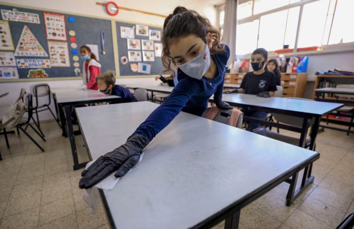 An Israeli pupil wearing protective gear sanitises her desk upon return to school after the COVID-19 lockdown, at Hashalom elementary in Mevaseret Zion, in the suburbs of Jerusalem, on May 3, 2020. - Israeli elementary schools were given the green light to bring back students of first through third grades, as the country looks to gradually transition back into a more normal routine after seven weeks of confinement measures. (Photo by Emmanuel DUNAND / AFP) (Photo by EMMANUEL DUNAND/AFP via Getty Images)