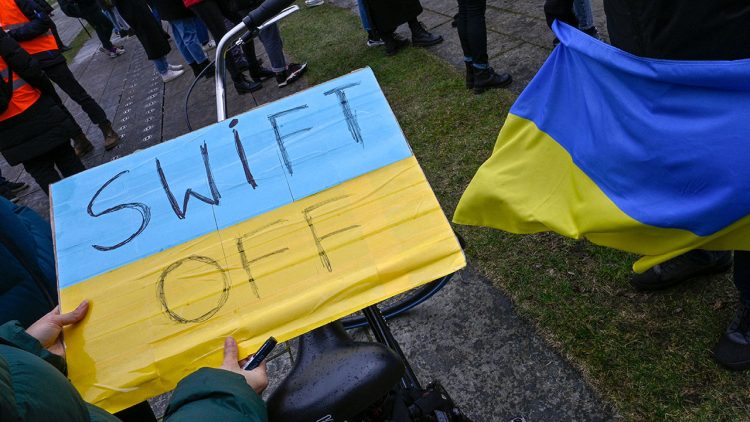 A demonstrator holds a placard reading "SWIFT OFF", refering to the international SWIFT financial transfer networkduring a protest against Russia's invasion of the Ukraine on February 25, 2022 in front of the Chancellery  in Berlin. (Photo by John MACDOUGALL / AFP) (Photo by JOHN MACDOUGALL/AFP via Getty Images)