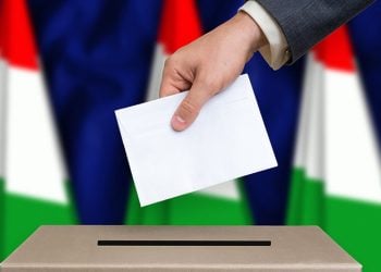 Election in Hungary. The hand of man putting his vote in the ballot box. Hungarian flags on background.