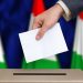 Election in Hungary. The hand of man putting his vote in the ballot box. Hungarian flags on background.
