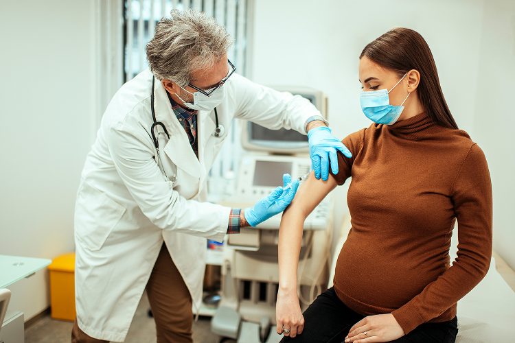 Pregnant woman getting vaccinated against flu or coronavirus. Male doctor giving an injection to pregnant patient while wearing face masks in the clinic.Credit: Getty