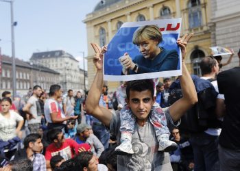 FILE - A migrant holds up a poster of German Chancellor Angela Merkel before starting a march out of Budapest, Hungary, towards Austria and Germany, Sept. 4, 2015. Merkel became the face of a welcoming approach to migrants as people fleeing conflicts in Syria and elsewhere trekked across the Balkans. More than 1 million asylum-seekers entered Germany in 2015-16.  (AP Photo/Frank Augstein, file)