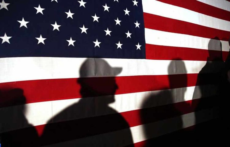 MYRTLE BEACH, SC - FEBRUARY 11:  Shadows are reflected on an American Flag as people line up to speak with Ohio Governor and Republican presidential candidate John Kasich at a restaurant in South Carolina following his second place showing in the New Hampshire primary on February 11, 2016 in Myrtle Beach South Carolina.  Kasich, who is running as a moderate, is expected to face a difficult environment in South Carolina where conservative voters traditionally outnumber moderates.  (Photo by Spencer Platt/Getty Images)