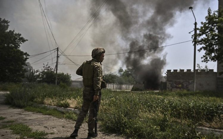 A Ukrainian serviceman stands in front of a burning vehicle during an artillery duel between Ukrainian and Russian troops in the city of Lysychansk, eastern Ukrainian region of Donbas, on June 11, 2022. (Photo by ARIS MESSINIS / AFP)