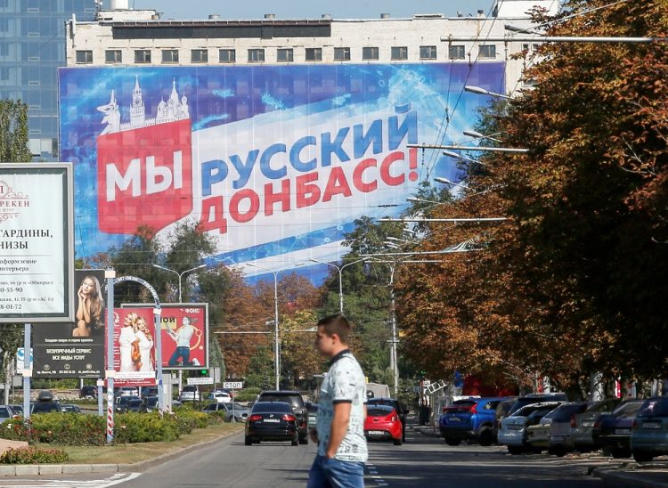 FILE PHOTO: A pedestrian crosses a street near a building with a banner displaying the slogan "We are Russian Donbass!" in the rebel-held city of Donetsk, Ukraine September 9, 2021. REUTERS/Alexander Ermochenko/File Photo