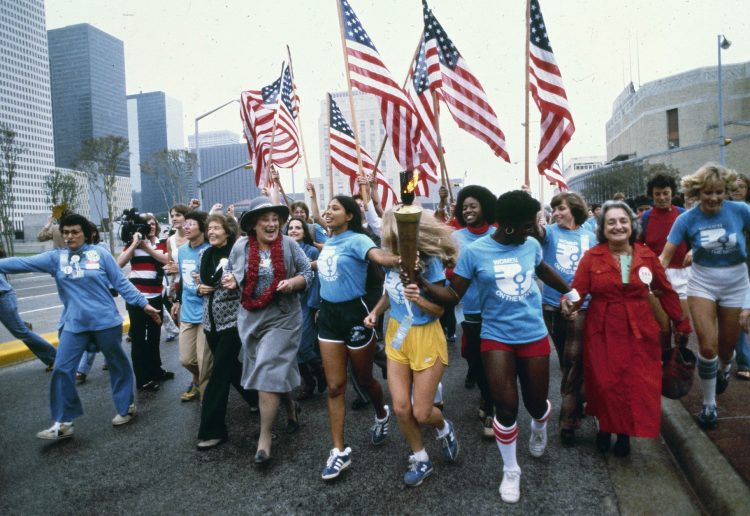 ADVANCE FOR USE MONDAY, JUNE 20, 2016 AND THEREAFTER -FILE - In this November 1977 file photo, leaders of the women's movement pass a torch that was carried by foot from New York to Houston, Texas for the National Women's Convention. Among the marchers, from left foreground are tennis star Billie Jean King, in blue shirt and tan pants; former U.S. Congresswoman Bella Abzug, wearing a hat; and feminist writer Betty Friedan, in a red coat. (AP Photo/Greg Smith)
