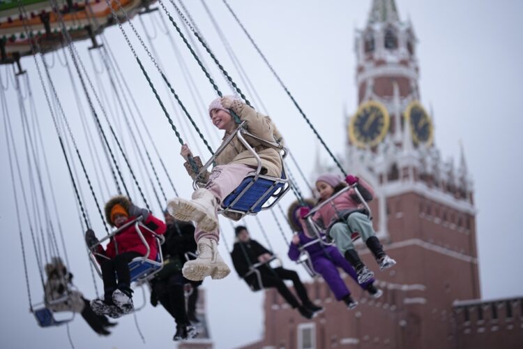 Children and their parents ride a carousel at a Christmas Market set up in Red Square decorated for the New Year and Christmas festivities with the Spasskaya Tower in the background in Moscow, Russia, Sunday, Dec. 17, 2023. (AP Photo/Alexander Zemlianichenko)