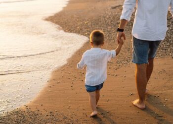 Happy Father's day. Father and baby play on the beach. Dad and him Child together enjoying sunset. Loving single father hugs cute little son.