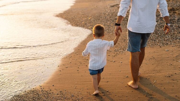 Happy Father's day. Father and baby play on the beach. Dad and him Child together enjoying sunset. Loving single father hugs cute little son.