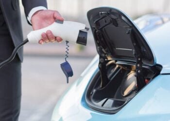 close-up photo of a male hand of a businessman charges an electric car, connects the charging cable