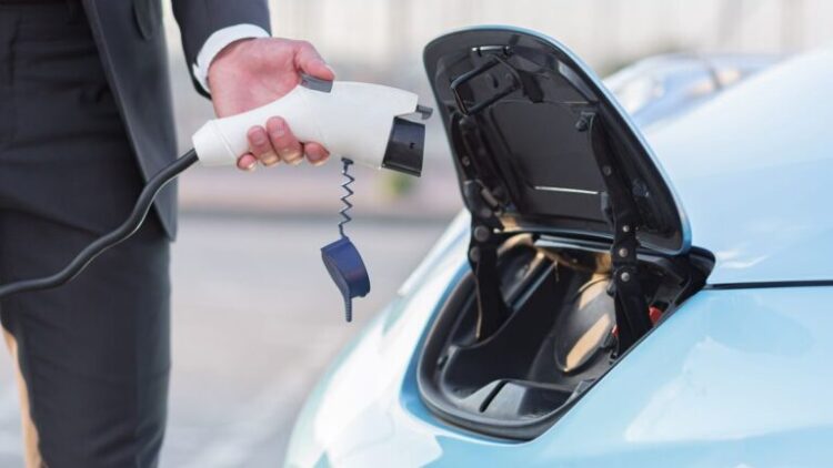 close-up photo of a male hand of a businessman charges an electric car, connects the charging cable