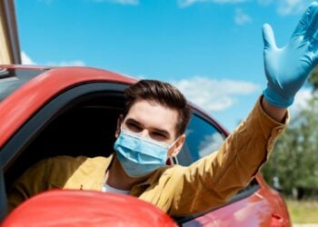 man in medical mask and protective gloves waving and driving taxi during covid-19 pandemic