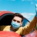 man in medical mask and protective gloves waving and driving taxi during covid-19 pandemic